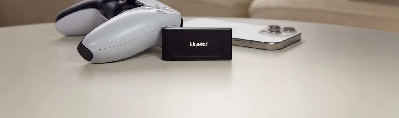 Kingston XS1000 black portable SSD on a tabletop beside a game controller and smartphone